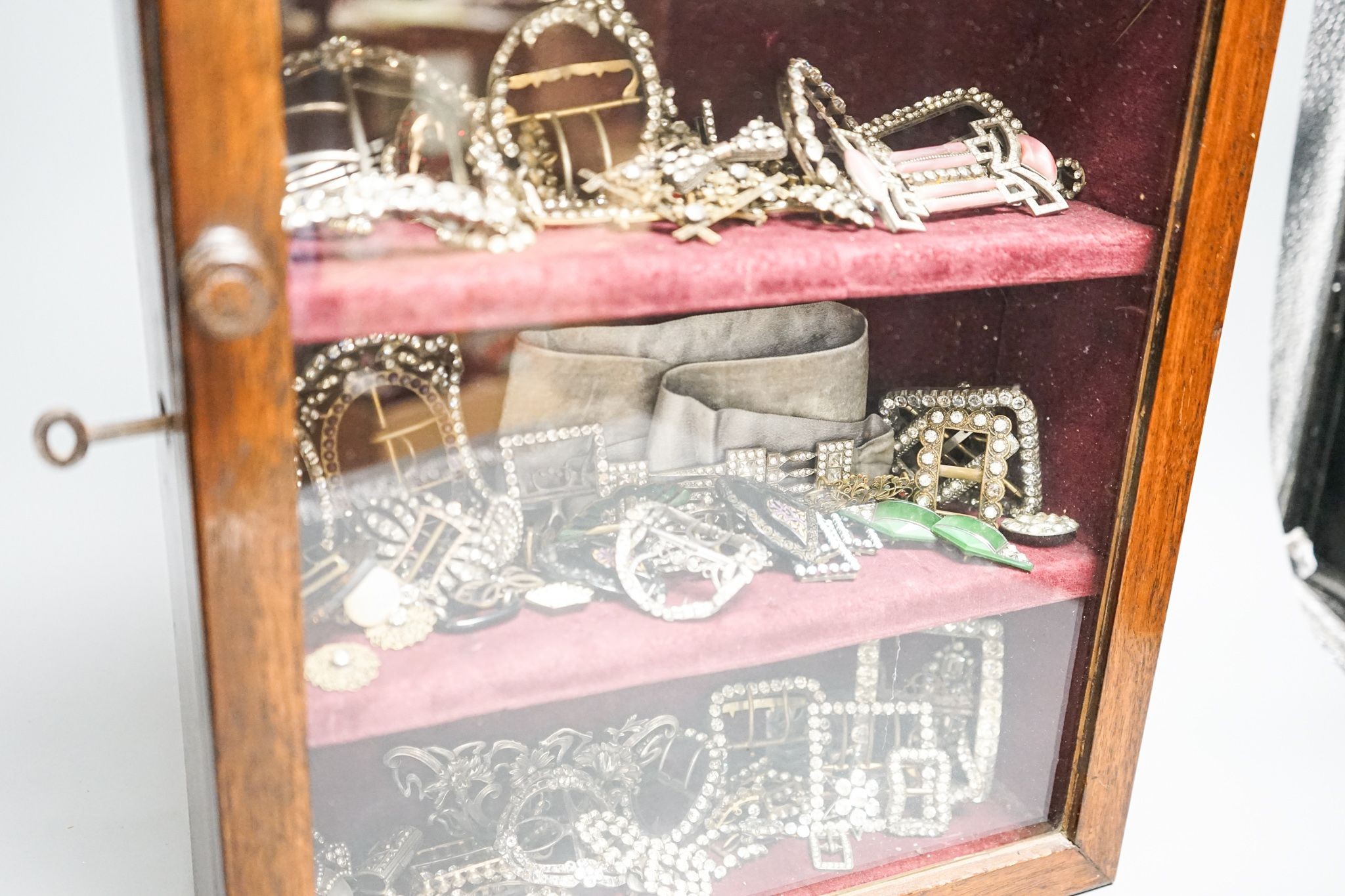 A large collection of 19th/20th century paste and enamel belt and shoe buckles and clips, contained in an oak display cabinet. 56cm
